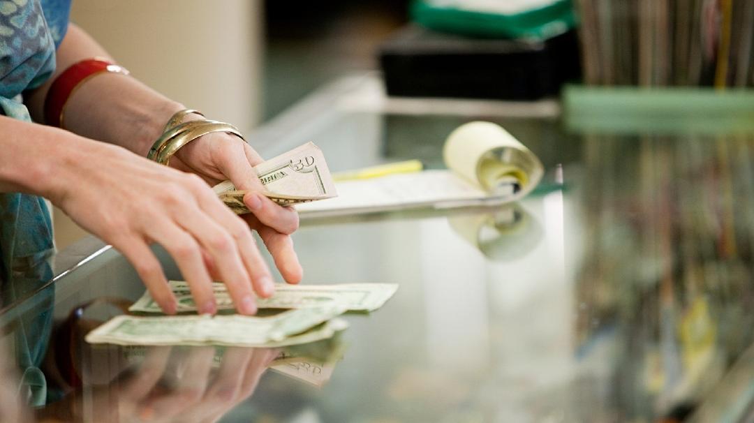 A person counting cash at a store counter, with a focus on their hands and the money.